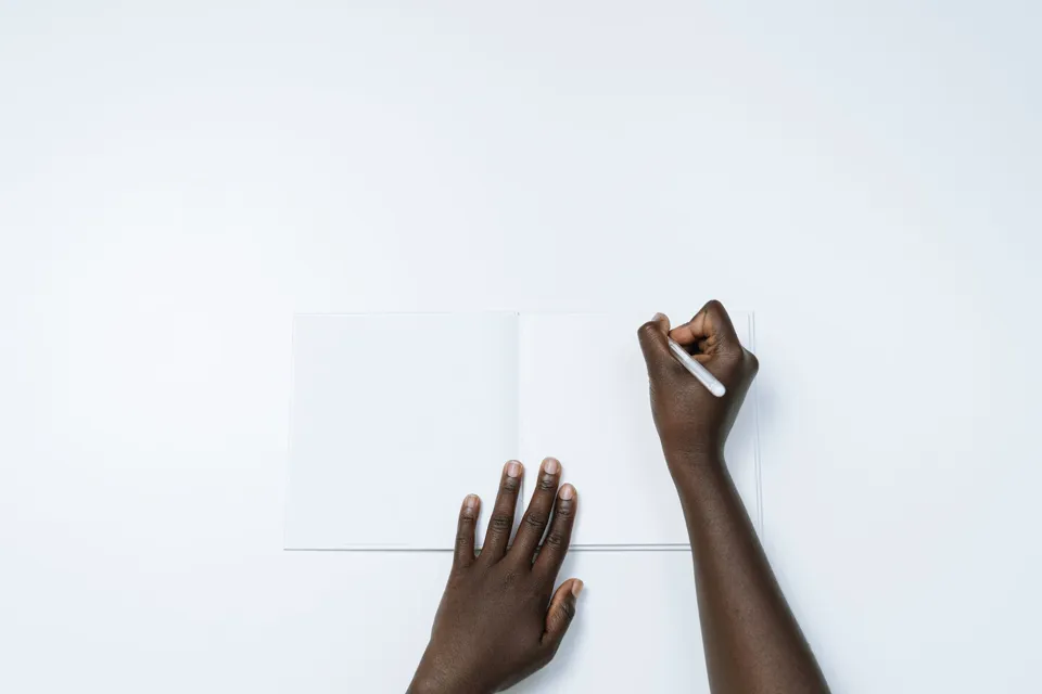 Main posée sur une page blanche, stylo en main