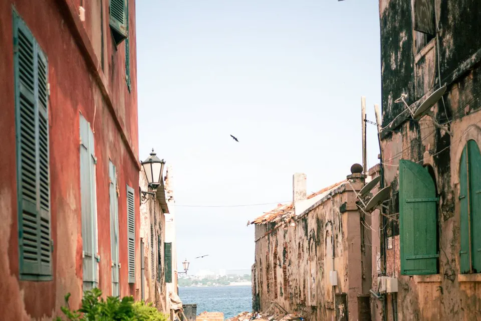 Ruelle de sable bordée de façades anciennes, ouvrant sur la mer, au Sénégal